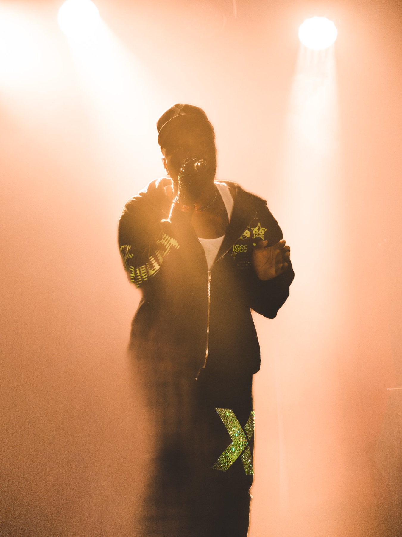 Performer backlit in a wash of warm haze, hand to the mic