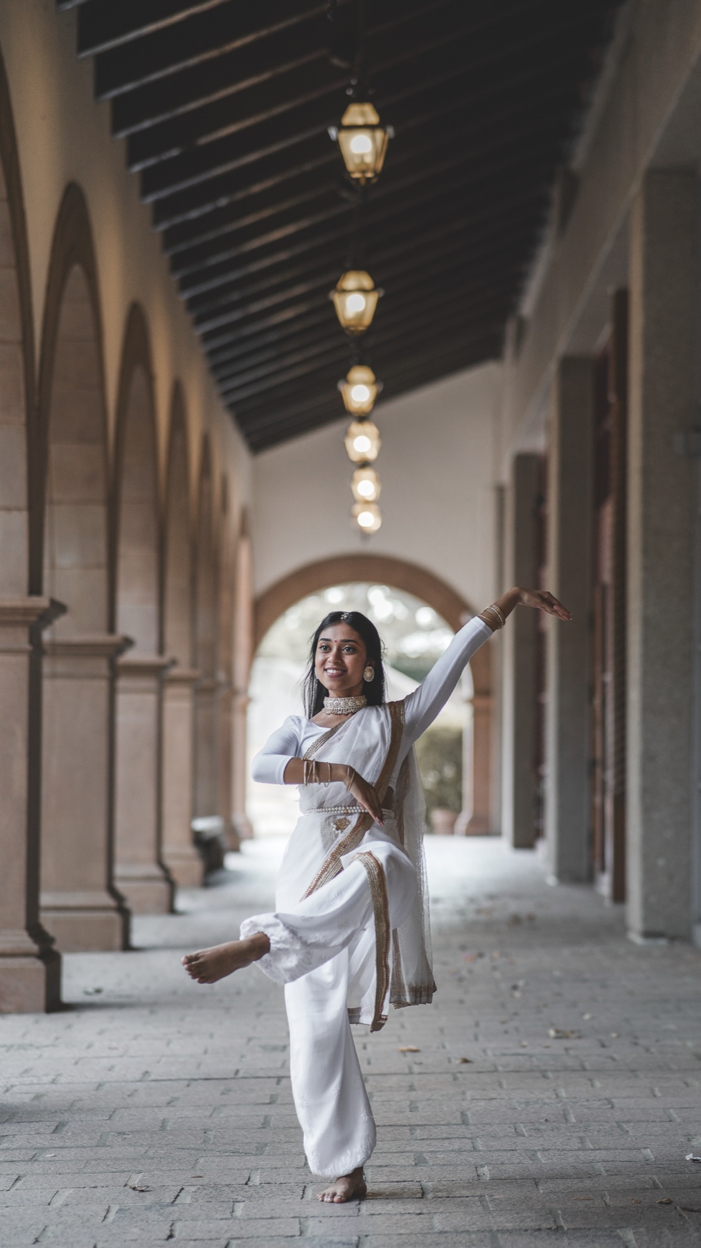 Classical dancer mid-movement in a sunlit colonnade