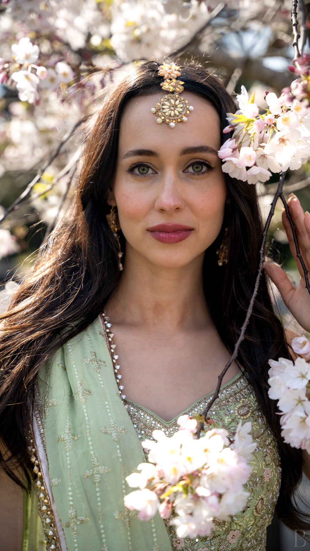 Portrait of Athenna Crosby, Miss World America 2024, in a green lehenga and maang tikka beneath cherry blossom