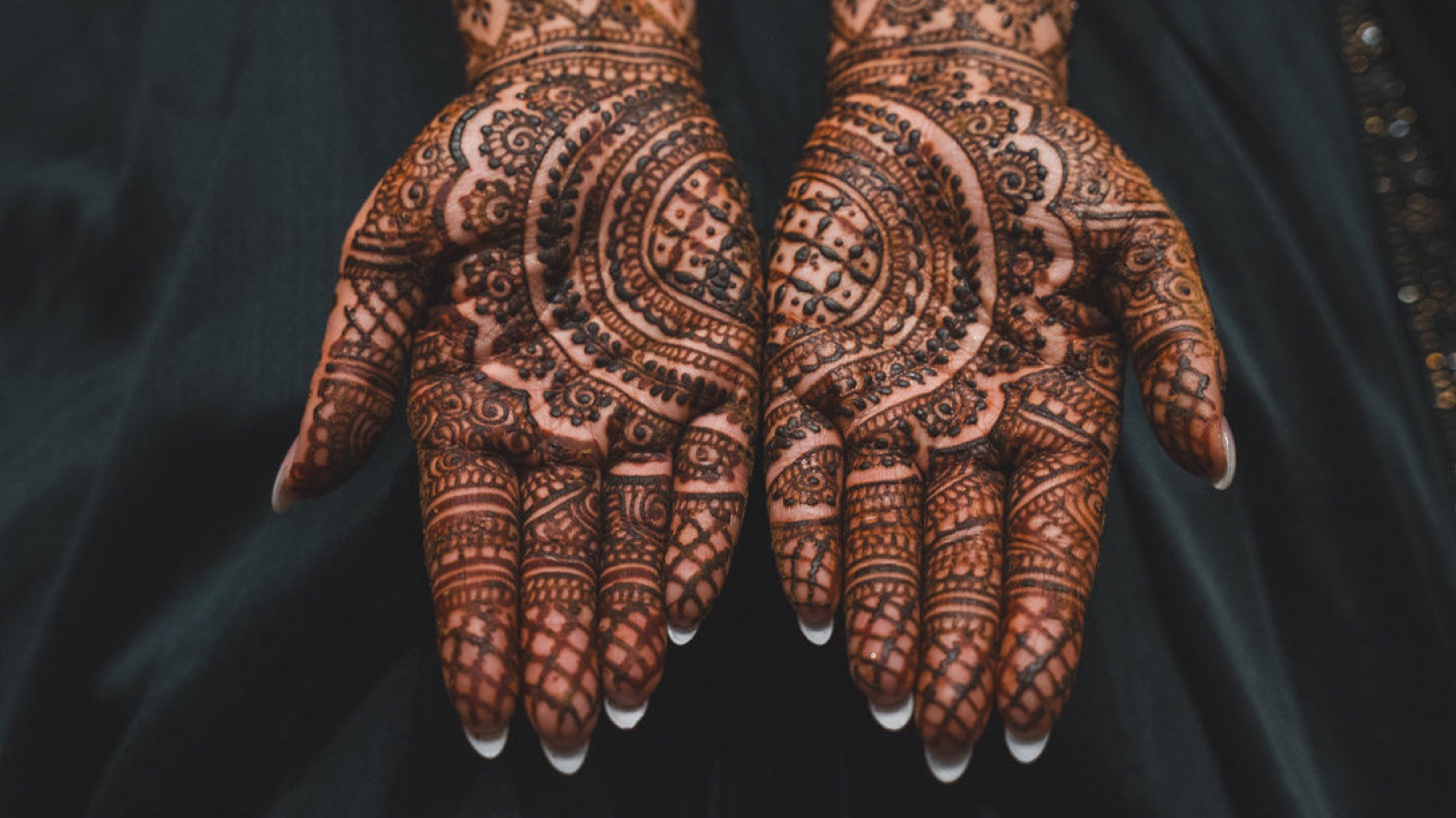 Two henna-covered palms held open against dark cloth