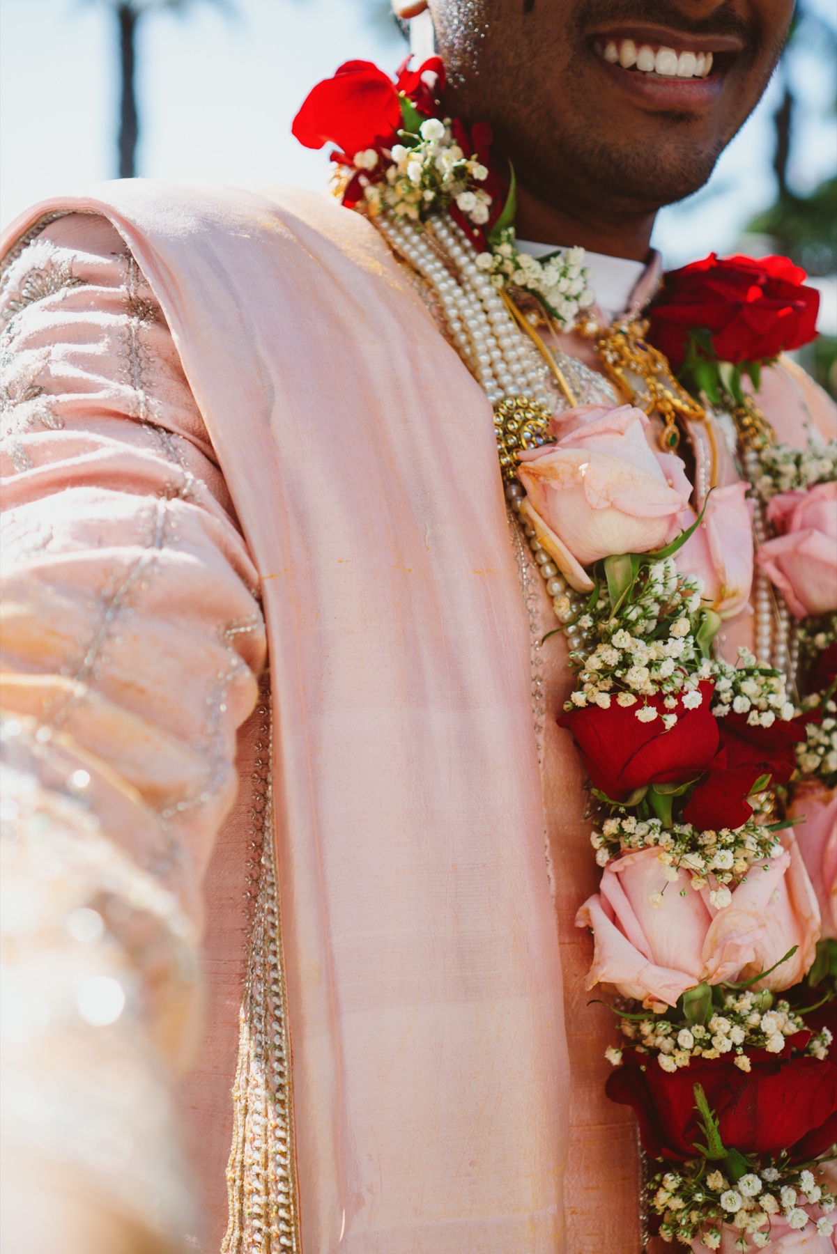 The groom laughing beneath a rose and jasmine garland