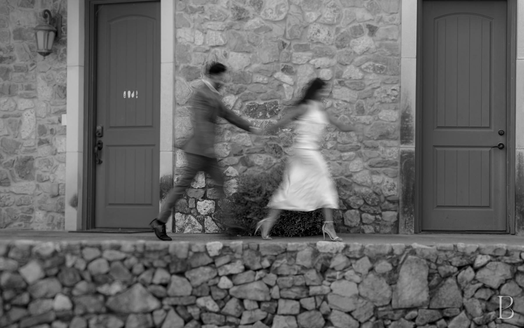 The couple walking past two teal doors in a stone wall, caught in motion blur