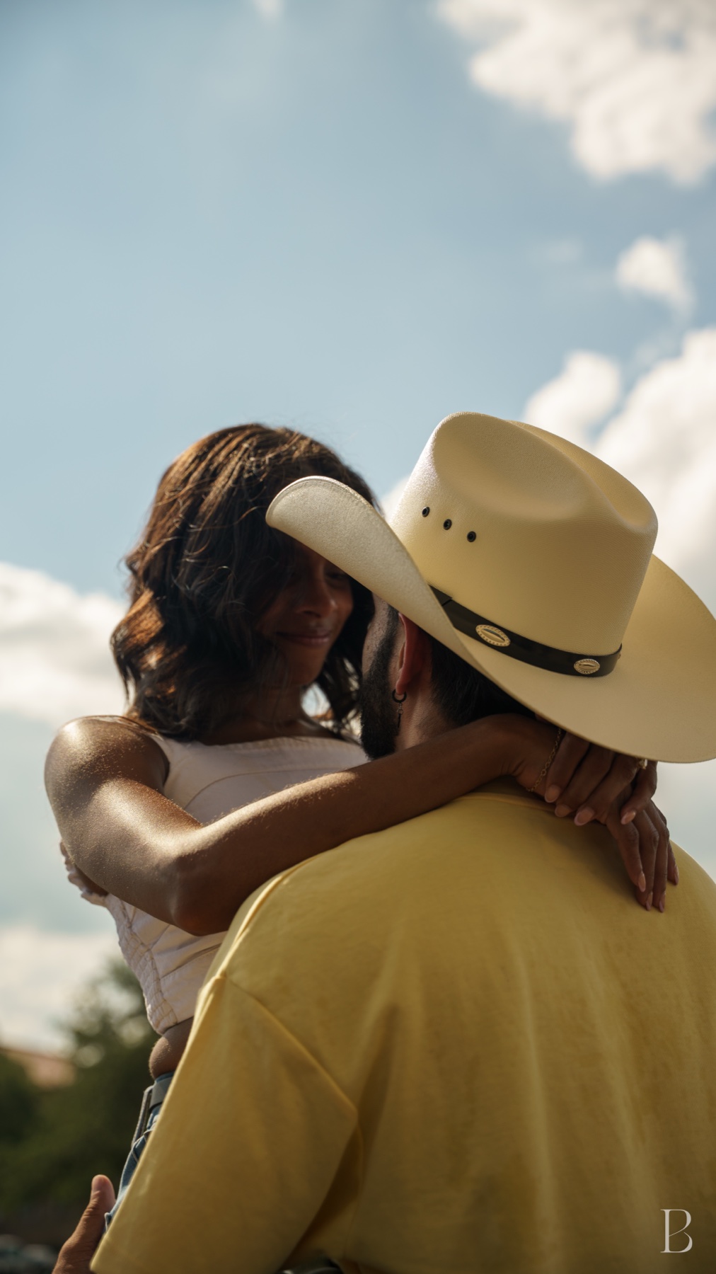 The couple close together under a wide sky, his hat shading her face