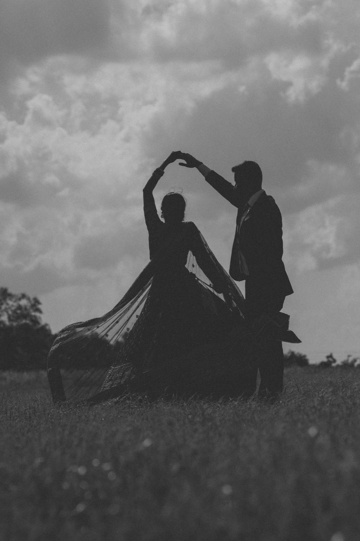 The couple in silhouette mid-twirl in an open field, black and white