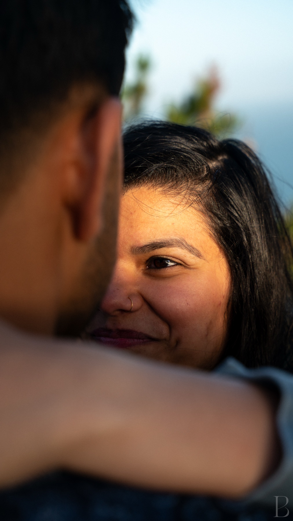 Her face over his shoulder in a close embrace at golden hour